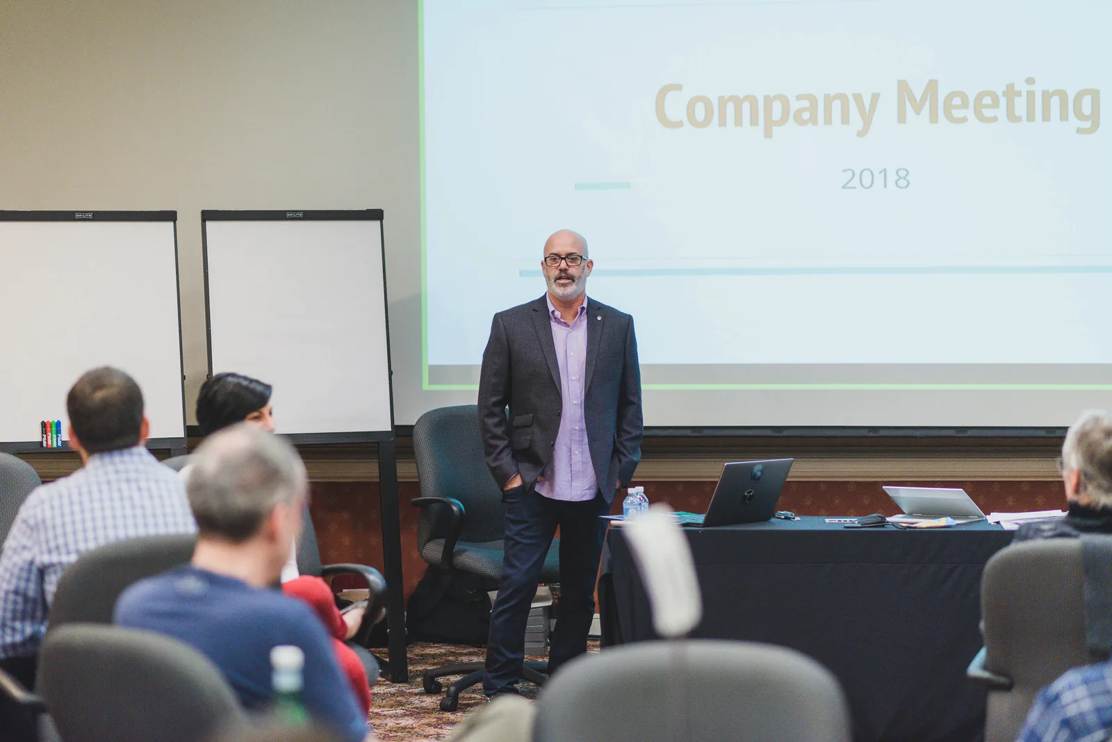 Ross Weinstein standing before seated colleagues at Voicebrook's annual company meeting, a slide reading 'Company Meeting 2018' projected behind him.